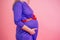 Close-up hands belly baby bump of a pregnant woman hug in a dress in studio on a pink background . concept of love for