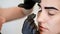 Close-up, the hands of the cosmetologist in black rubber gloves hold a cotton swab and correct the shape of the eyebrows