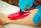 Close-up hands of cosmetologist in blue gloves applying red, berry flavor paste for sugaring