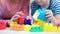 Close-up hands of female child psychologist and little boy playing with colored cubes during testing