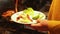 Close up of hands getting grilled fried food of vegetables, meat sausages and salad with spoon into plate from saucepan