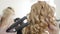 Close-up of hands of hairdresser working with curls of redhead client in beauty salon. Rich young Caucasian woman