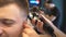 Close up hands of hairstylist cutting hair of young client with electric razor in barbershop. Arms of barber making male