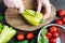 Close up of hands holding a knife and sweet green peppers on an oval wooden chopping Board that lies on a wooden table with