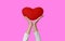 Close up hands of little child girl lift up red heart isolated on pink background