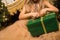 Close up. Hands of a little girl in a golden dress tied / untied the ribbon on a gift box in a green package. Copy space