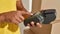 Close up of hands of male mover using terminal for payment with credit card, standing near a stack of cardboard boxes