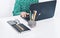 Close-up of hands middle-aged woman in green blouse typing on keyboard laptop, concrete holder with pencils and pens, notebook,