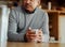 Close up of hands of pensive retired biracial elderly male leaning on modern kitchen counter, holding morning coffee in