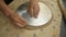 Close-up of the hands of a Potter who cuts off excess white clay, making a blank for the future plate.