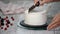 Close up of hands smearing butter cream on chocolate cake by white spatula.