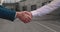 Close up of the hands of top managers in business suits, shake hands with each other, near building background, agree to