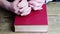 Close-up of the hands of two men, young and old, folded in a prayer gesture on a thick family bible in a dark red cover, the