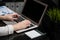 Close-up of hands typing on laptop with blank black screen next to charts and calculator