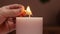Close-up hands of unrecognizable man lighting large white candle with match, side view.