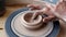 Close-up hands of unrecognizable potter making ceramic cup with dirty arms on twisted pottery wheel in pottery workshop