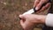 Close-up hands of unrecognizable tourist male brushing the blade of his knife off the ground at outdoors.