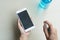 Close up hands of woman disinfecting smart phone by spraying alcohol from a bottle, protection against infectious virus, bacteria