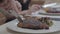 Close up hands of young man in the foreground and woman in the background cutting tasty steak lying on the plate with