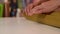 Close-up hands of young woman carefully applying double-sided tape to golden wrapping paper to package festive cardboard