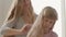 Close-up hands of young woman combing hair of her blond daughter. Concept of motherhood, childhood, one parent. Leisure