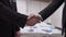 Close-up handshake of two Caucasian businessmen in office indoors. Unrecognizable men in black formal suits shaking