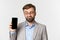 Close-up of handsome businessman in gray suit and glasses, looking at mobile phone screen intrigued, standing over white