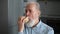 Close-up of handsome gray-haired mature adult male eating unhealthy food enjoying dinner at home. Hungry bearded senior