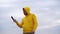 Close up of handsome man in hood talks on smartphone in hilly terrain. Adult male in yellow hoodie gets great news and