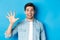 Close-up of handsome man smiling, showing fingers number five, standing over blue background