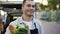 Close up handsome smiling courier man going from the car to house and holding paper bag with food outdoors. Worker