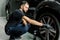 Close up of handsome young male employee worker cleaning the wheel rim of modern black crossover car by scrubbing brush