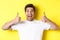Close-up of handsome young man showing thumbs up, approve and agree, smiling satisfied, standing over yellow background