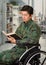 Close up of a handsome young soldier sitting on wheel chair reading a book at home, in a blurred background
