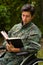 Close up of a handsome young soldier sitting on wheel chair reading a book in the patio, in a backyard background