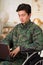 Close up of a handsome young soldier sitting on wheel chair using his computer over his legs, wearing military uniform