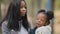 Close up happy african american family smiling in park little girl talking with woman baby holding teddy bear portrait