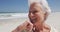 Close up of happy senior caucasian woman with hand on chin sitting on the beach enjoying the view