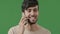 Close up happy smiling young arab guy in studio on green background talking using smartphone surprised positive man