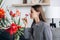 Close up of happy smiling young caucasian woman sniffs fresh red flowers sitting alone on cozy sofa at home. Portrait satisfied