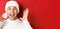 Close-up of happy young man in santa hat, making big christmas announcement, smiling amazed, standing over red