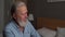 Close-up headshot of gray-haired handsome mature adult male with beard talking with somebody sitting on bed at home.