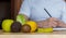 Close-up of healthy fruits and vegetables, with a nutritionist writing in the blurred background. Lemon, kiwi, apple, lettuce,