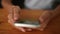 Close-up high-angle view of unrecognizable young woman using smartphone, texting messages sitting at desk. Closeup