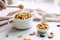 Close up of homemade honey caramel cornflakes in white bowl with cashew nut, pumpkin seeds and dried raisins on white wooden