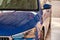 Close up hood and headlight of a blue car in a drops of water after car washing. Clean car after high pressure water