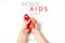 Close up horizontal image of child`s hands holding red ribbon on white background, HIV awareness concept, world AIDS day.