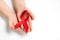 Close up horizontal image of child`s hands holding red ribbon on white background, HIV awareness concept, world AIDS day.