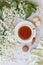 Close-up of hot cup of tea with sweet macaroons surrounded by beautiful white flowering apple tree branches on a gray background.