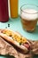 Close up of hot dog with corn, glass of beer and bottles with mustard and ketchup on blue.